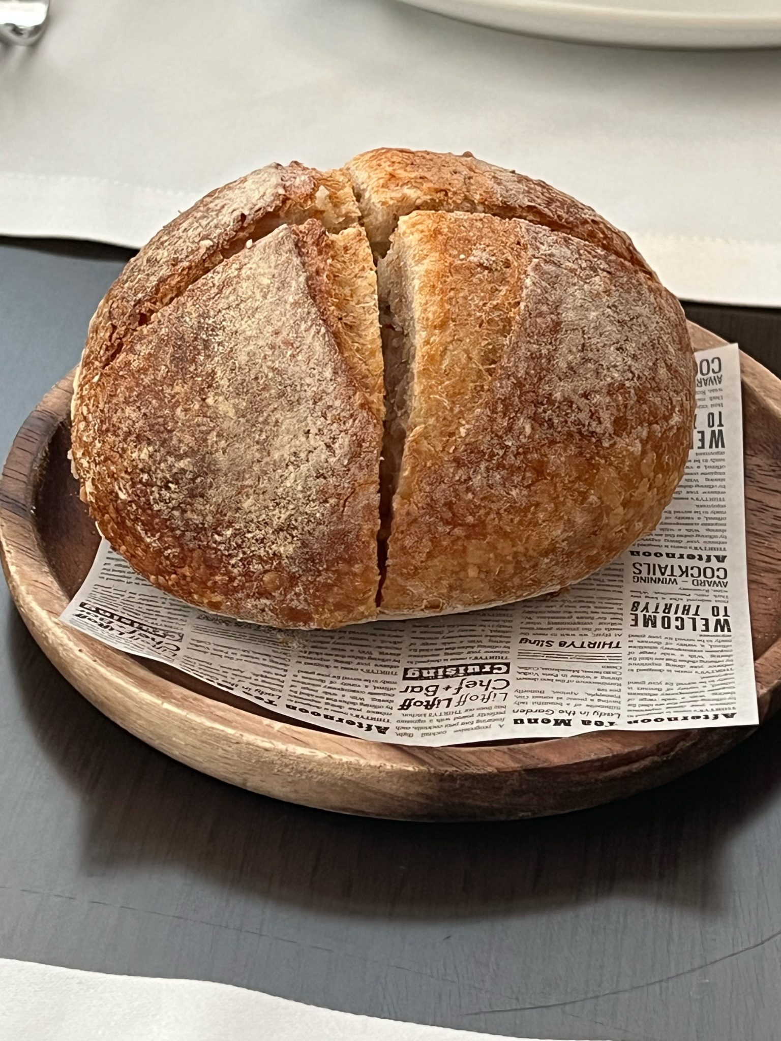 A round loaf with a cross cut into the crust, on a wooden plate.